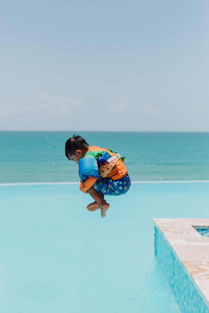 A young boy wearing a life jacket jumps into a pool. 