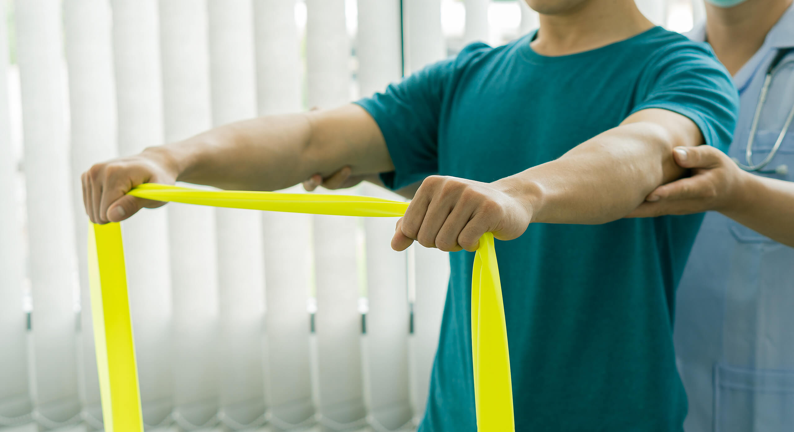 A man uses a resistance band during physical therapy for his shoulders.
