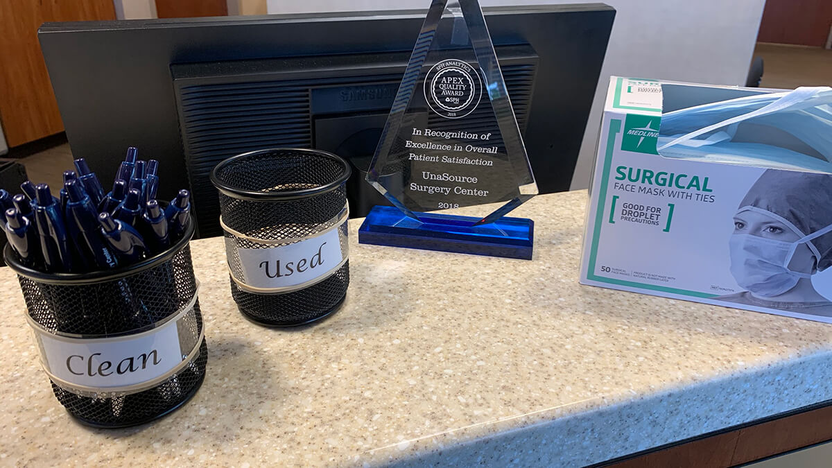 UnaSource Surgery Center is taking extra measures to prevent the spread of COVID-19. This is an image of surgical face masks on a desk along with a cup of "clean" and "used" pens.