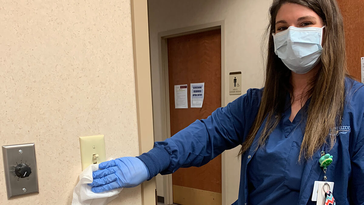 UnaSource Surgery Center is taking extra measures to prevent the spread of COVID-19. In this image, a staff member is using a disinfecting wipe to clean a light switch.