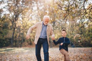 Chronic leg pain or back pain can be alleviated with the HF10 spinal stimulator by Nevro. In this image, a man and his grandson walk in the park on an autumn day while kicking up the leaves.