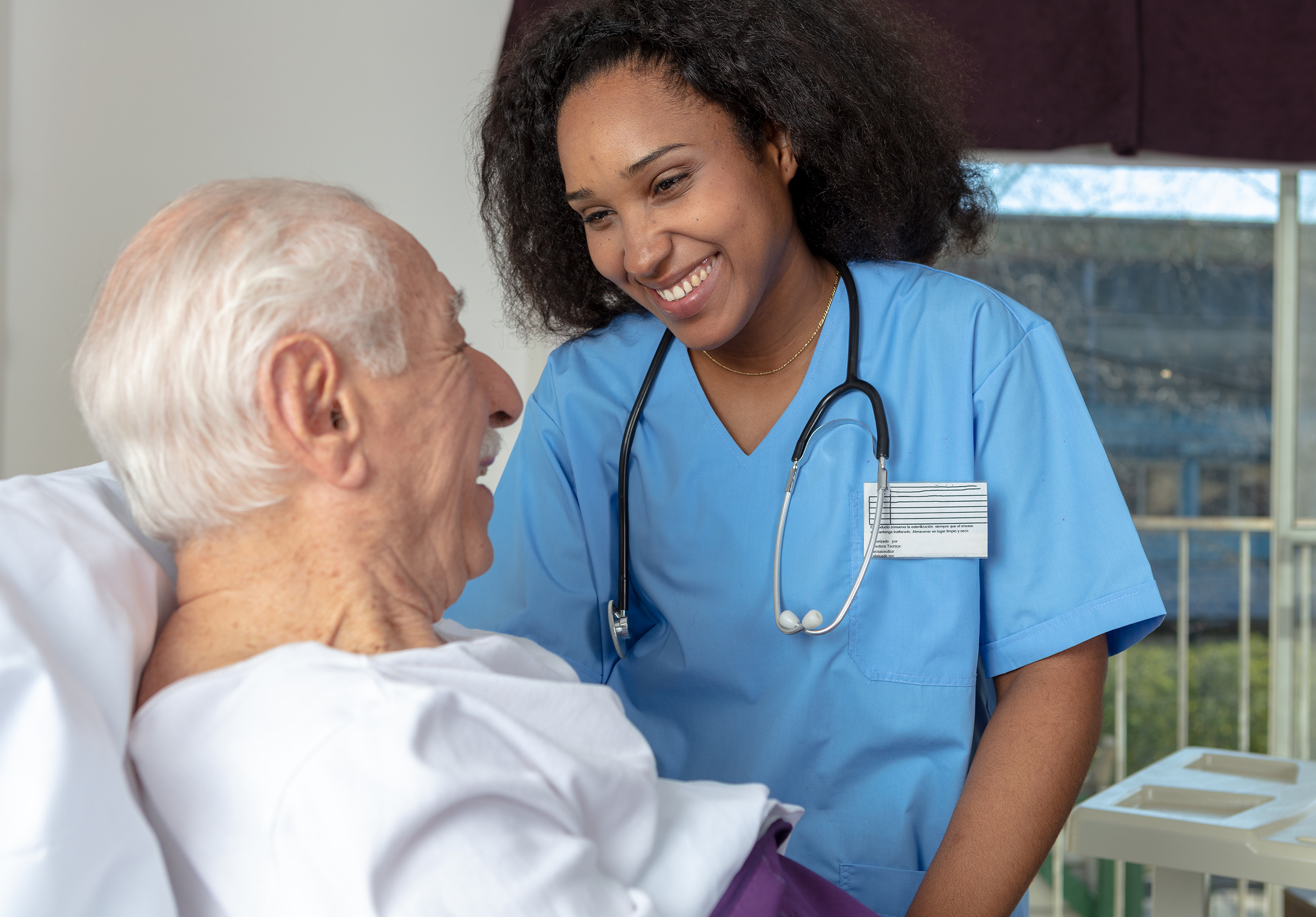 Our outpatient surgery center anesthesiologists and nurse anesthetists practice opioid-free anesthesia on a regular basis with peripheral nerve blocks and other solutions. In this image, a smiling nurse speaks with a patient, who is in a bed.